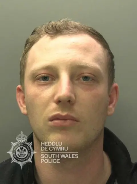 South Wales Police Thomas Morgan mugshot in police custody, looking towards the camera, wearing a dark top