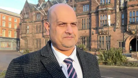Abdul Khan, dressed in a suit, stands outside Coventry City Council House.