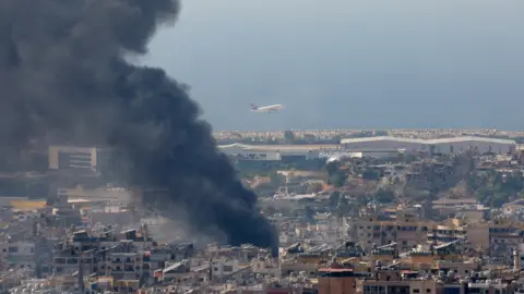 Reuters Een vliegtuig stijgt op vanaf de luchthaven van Beiroet terwijl rook opstijgt uit de zuidelijke buitenwijk van de stad na een Israëlische luchtaanval (8 oktober 2024)