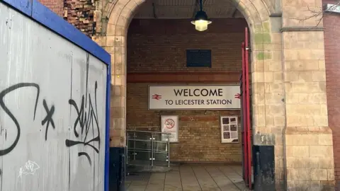 Building site hoardings next to a sign saying "Welcome to Leicester station"