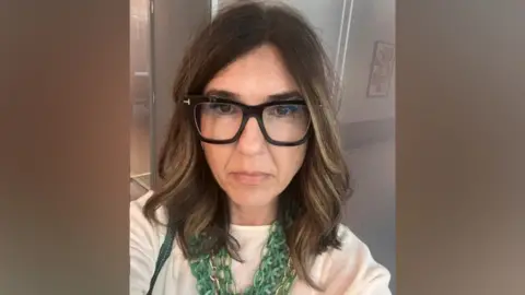 Filomena Gianfrancesco, a woman in glasses and a green necklace takes a selfie. She has brown hair.