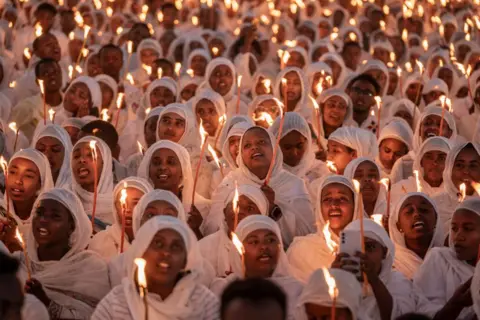 Getty Images Para jamaah memegang lilin dan menyanyikan lagu keagamaan saat mereka berkumpul pada malam perayaan Natal Ortodoks Ethiopia di Gereja Bole Medhanialem di Addis Ababa pada 6 Januari 2025. 