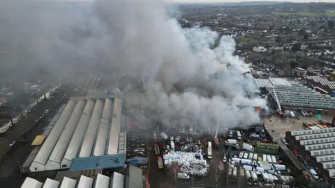 Aerial view of a large plume of grey smoke emitting from a factory