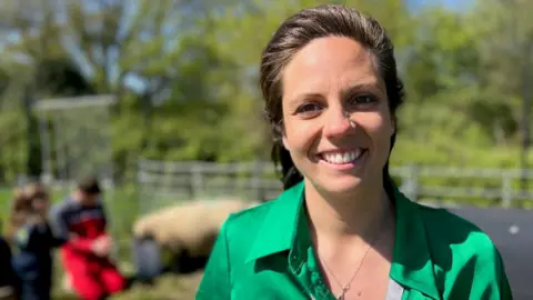 BBC/Sam Dixon-French A woman with black hair and a green top smiles at the camera.