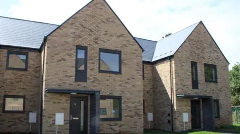 A row of newbuild brick homes. They have black doors and black framed windows. 