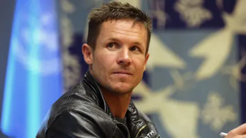 Felix Baumgartner looks off to the side. He has blue eyes and short brown hair. He is wearing a leather jacket.