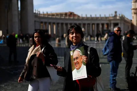 Reuters A person holds an image of Pope Francis in St. Peter's Square, at the Vatican, on 26 February 2025
