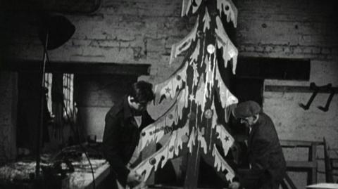 Two men hold a Christmas tree prop
