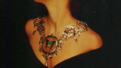 Gold Lark Jewellery An elaborately-designed silver necklace with a taxidermy butterfly pendant hanging around a woman's neck