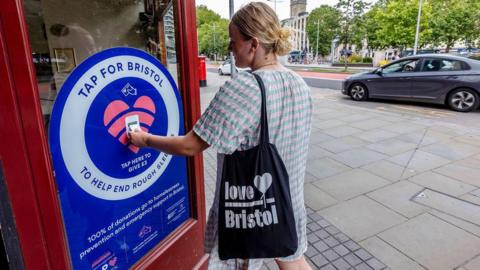 A woman in a pale dress using a contactless donation point in Bristol