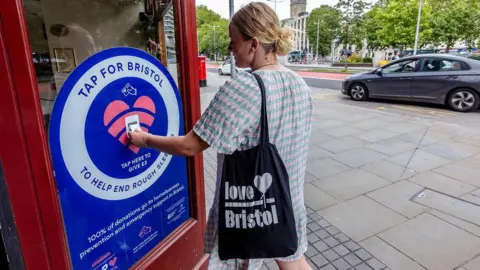 Plaster Communications A woman in a pale dress using a contactless donation point in Bristol