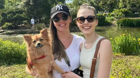 PA Media Kim Ward and Shannon Foley. Irish passengers who had planned to travel home via the storm-damaged Holyhead ferry port this Christmas. They are standing in a sunny park with their dog Ziggy.