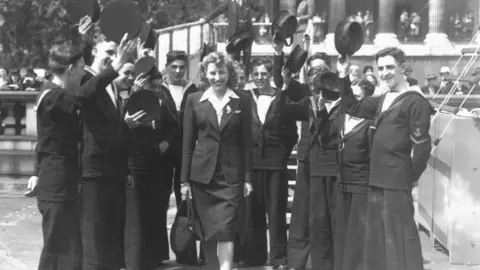 Getty Images A black and white photo from 1943 showing Dame Vera in Trafalgar Square, London, surrounded by people from the Navy in uniform and taking their hats off.