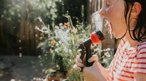 Getty Images A little girl sprays water directly into her mouth using a hosepipe - stock photo A child attempts to cool off on a very hot day using a hose pipe. She sprays water directly into her mouth.