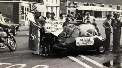 Allan Brew A black and white image of members of the supporters club standing out in the street to fundraise. They have a car with the sign 'rescue helicopter' written on it.