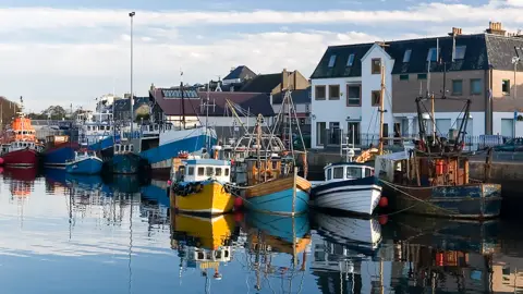 Getty Images Boats moored in Stornoway Harbour on a clear day with houses in the background