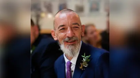 Family handout An elderly man with a shaved head and grey beard wears a navy blue suit.