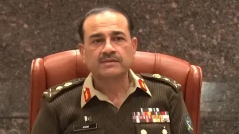 ISPR/X General Syed Asim Munir, wearing a military uniform, sits on a chair. He has many medals pinned on his uniform.