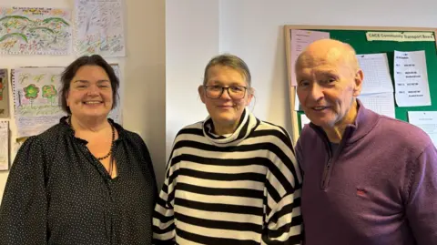 CACE staff members Susan, who has dark hair and is wearing a black blouse with white spots, Lindsay, who has blonde hair, tied back, who is wearing a black and white striped polo-neck jumper and George, who has a bald head and is wearing a maroon top. They are all smiling at the camera.