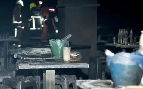 Tables and chairs are covered in ash at the scene of a fatal fire at a bar in Bangkok