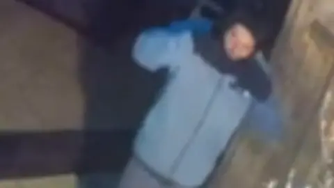 Gloucestershire Police CCTV footage shows James Brown outside someone's property at night. He is wearing a blue jacket and a face covering which has slipped off.