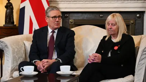 PA Media The PM, wearing a dark suit, chats with Margaret Aspinall, also wearing black clothes. She wears a circular red Hillsborough campaign badge.