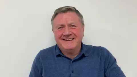 Kate Moser Andon/BBC Dennis Jones headshot, wearing a blue polo shirt, smiling.