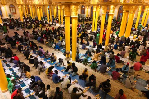 Cem Ozdel / Getty Images Hundreds of people sit down on the floor to eat together at long, identically laid out tablecloths