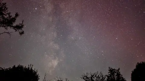 Graeme Healey A night sky filled with stars and a soft red glow in the Cotswolds