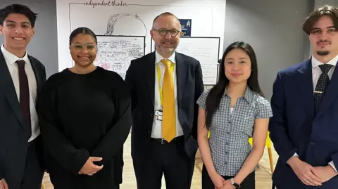 BBC Jai, Anya, Alex Crossman, Kami and Ismael stand in a line and smile at the camera. 