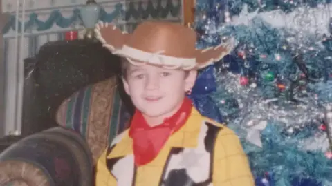Family handout A photograph of Kaine Fletcher as a child, wearing a Woody costume from Toy Story', standing in front of a Christmas tree