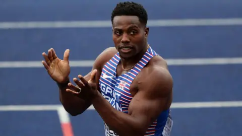 The image shows an athlete in Team GB uniform, mid-clap on a track.