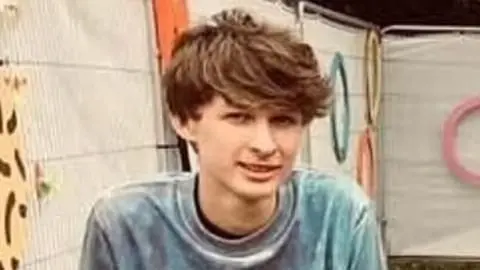 BBC Dylan Thomas who has floppy brown hair and is wearing a grey t shirt, smiling at the camera 