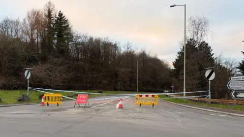 A police cordon is in place at the entrance to a road, with a 'road closed' sign and traffic cones also in place. Signs say Treorci, Clydach Vale, Cwm Clydach, Llwynpia and Tonypandy.