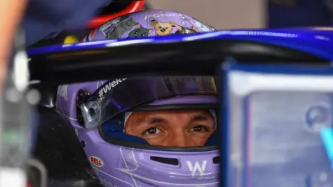 Getty Images A close-up photo of Alex Albon while sat in his F1 car. He's wearing a light purple helment and you can make out that there are some cartoon images of cats around the top of the helmet. His eyes and the top of his nose are visible as the helmet visor is lifted up.