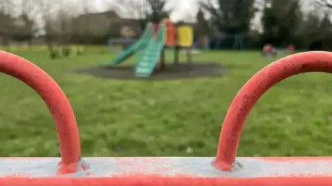 A playground with red fence and a slide in the background 