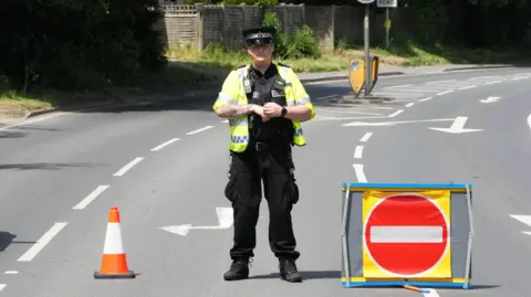 Eddie Mitchell A police officer stood in the middle of a road, with a road closed sign next to him.