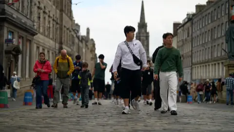 Tourists on Edinburgh's Royal Mile, with the large brown buildings on either side of the cobbled streets