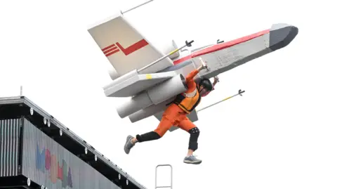Daniel Mazzei participates in the Birdman Rally during the Moomba festival's Birdman Rally in Melbourne, Australia. He is wearing an orange outfit and has a plane shaped device attached to him
