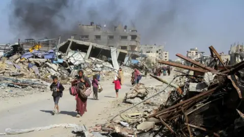 Reuters women and children walk past the smouldering wreckage of buildings in Gaza