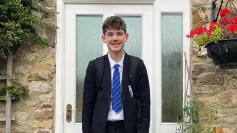 Charlie Vart, wearing school uniform, stood outside a cottage front door 