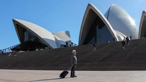 ABC News/Declan Bowring Terry Harper standing with a suitcase outside the Opera House