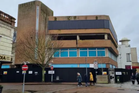 MACE The building before it was refurbished into a library. It stands three storeys tall and has black boarding preventing people from entering. 