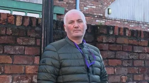 POLICE SCOTLAND Gary Nicol leaning against a brick wall wearing a green jacket and purple lanyard.
