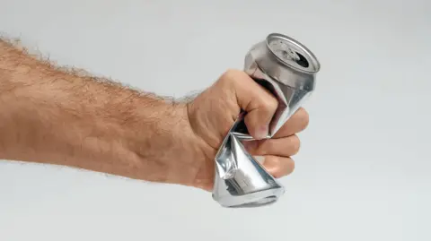 Male hand squeezing and crushing empty aluminum beverage can on gray background. Symbolic gesture expressing stress, frustration, anger or emotional pressure.