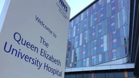 Exterior of the Queen Elizabeth University Hospital in Glasgow with a large welcome sign in the foreground and building in the background.