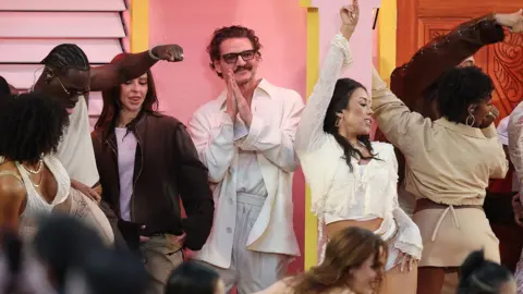 Getty Images Pedro Pascal dances as Bad Bunny performs. Pedro is seen in a white suit and is smiling 