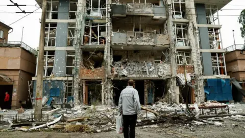 Reuters A resident looks at an apartment building that was damaged in a Russian drone strike, amid Russia's attack on Ukraine, in Kyiv.