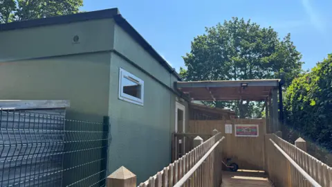 Harry Stevens/BBC A green school building with a wooden decking walkway and a canopy over the entrance 