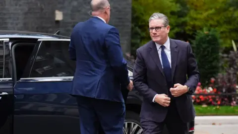 PA Media Keir Starmer walks out of his Prime Ministerial car outside No 10 Downing Street. He in correcting his suit blazer whilst his assistant closes the door behind him